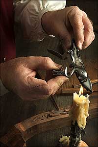 Gunsmith George Suiter soots a brass lock with a guttering candle.