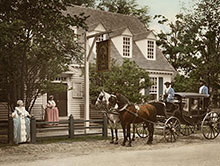 Colorized black-and-white photograph showing women in gowns and men driving a carriage.
