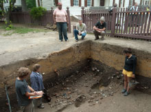 Archaeologists stand above and inside an excavation.
