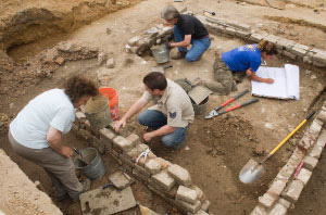 Four archaeologists examine brick foundations.