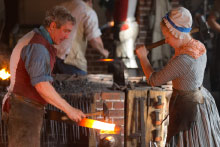 Two blacksmiths pound heated iron.